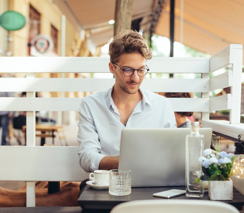 Ein junger Mann sitzt an seinem Laptop und einem Kaffee in einem Café. 