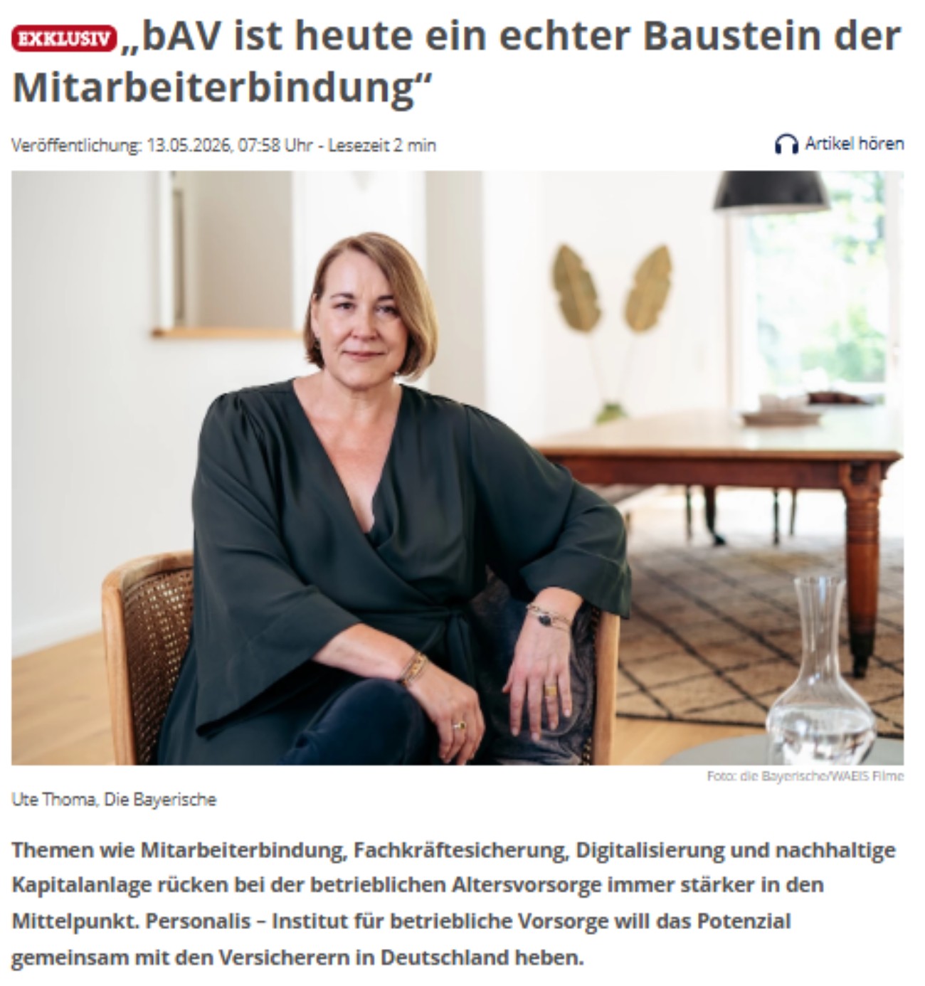 Porträt einer sitzenden Frau mit kurzem blondem Haar in dunkler Kleidung in einem hellen Wohnraum. Sie blickt direkt in die Kamera, im Hintergrund stehen ein Holztisch, dekorative Pflanzen und eine Karaffe auf einem Teppichboden.<br/>